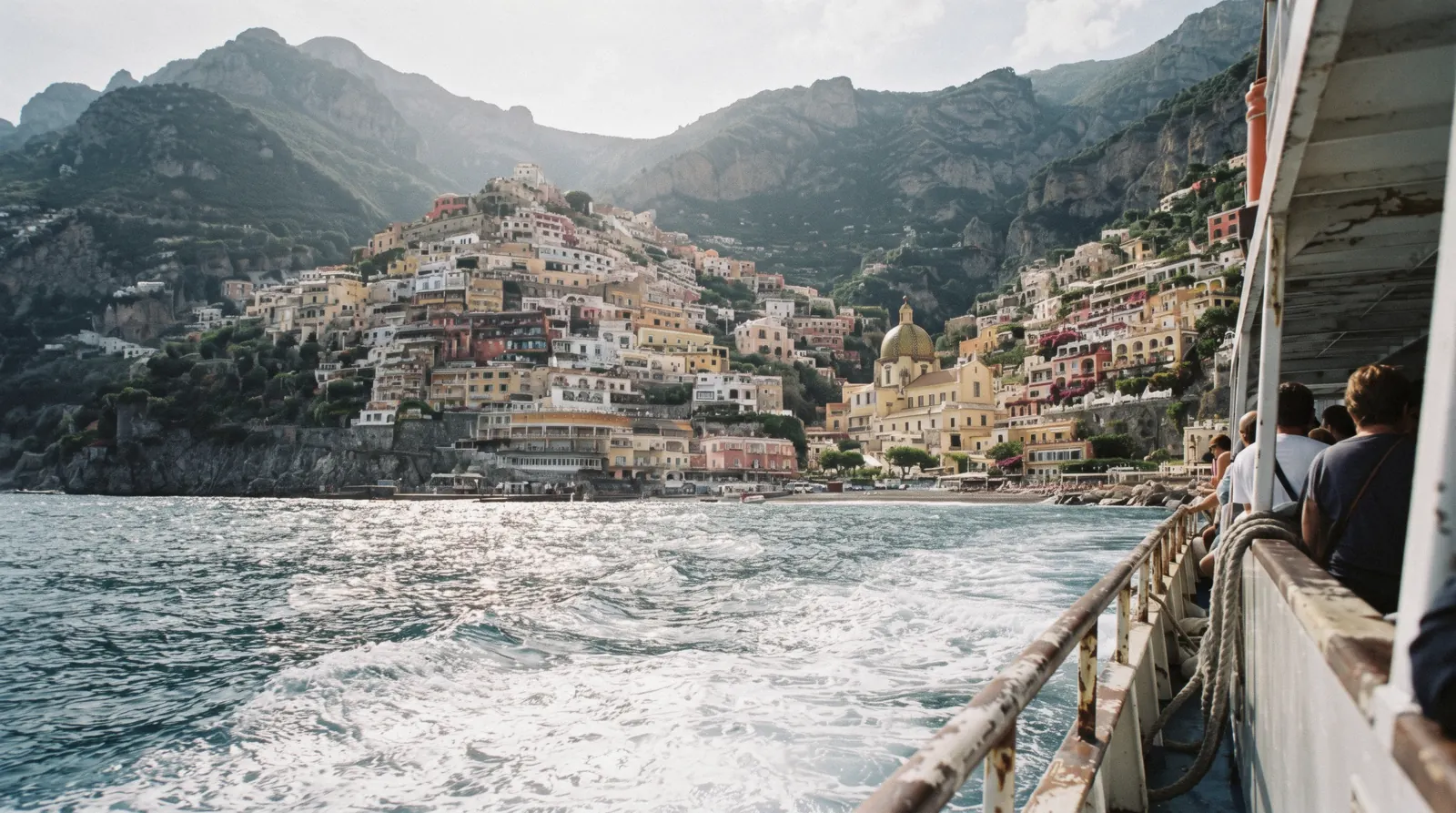 The stacked pastel houses of Positano above the sea with a ferry wake in the foreground