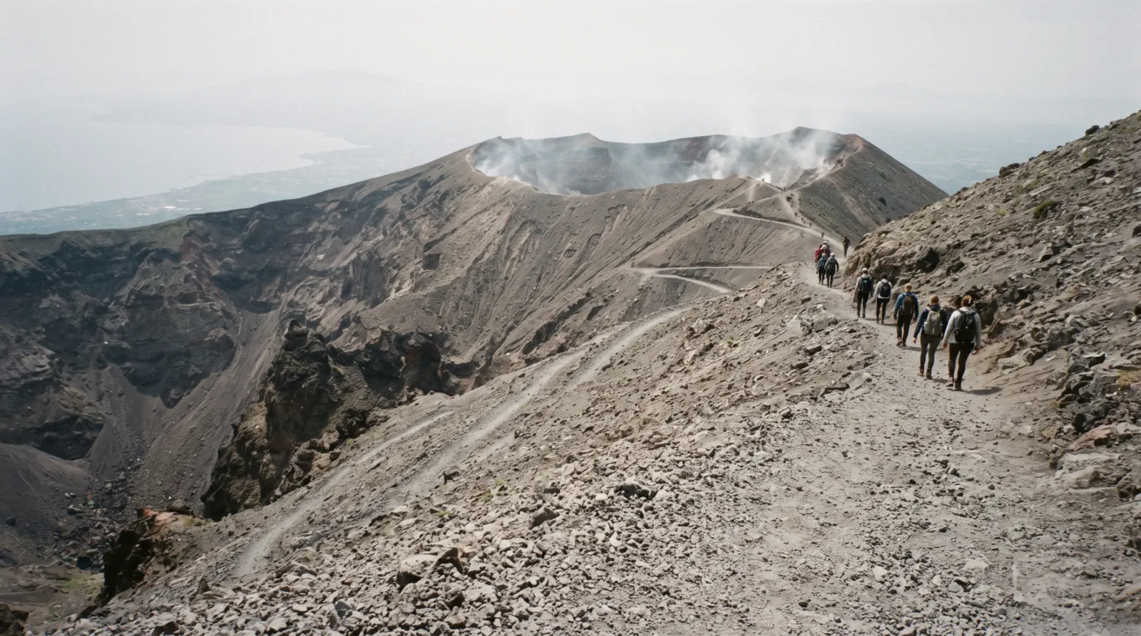 The crater rim of Mount Vesuvius with steam rising from the rock and the Bay of Naples hazy below
