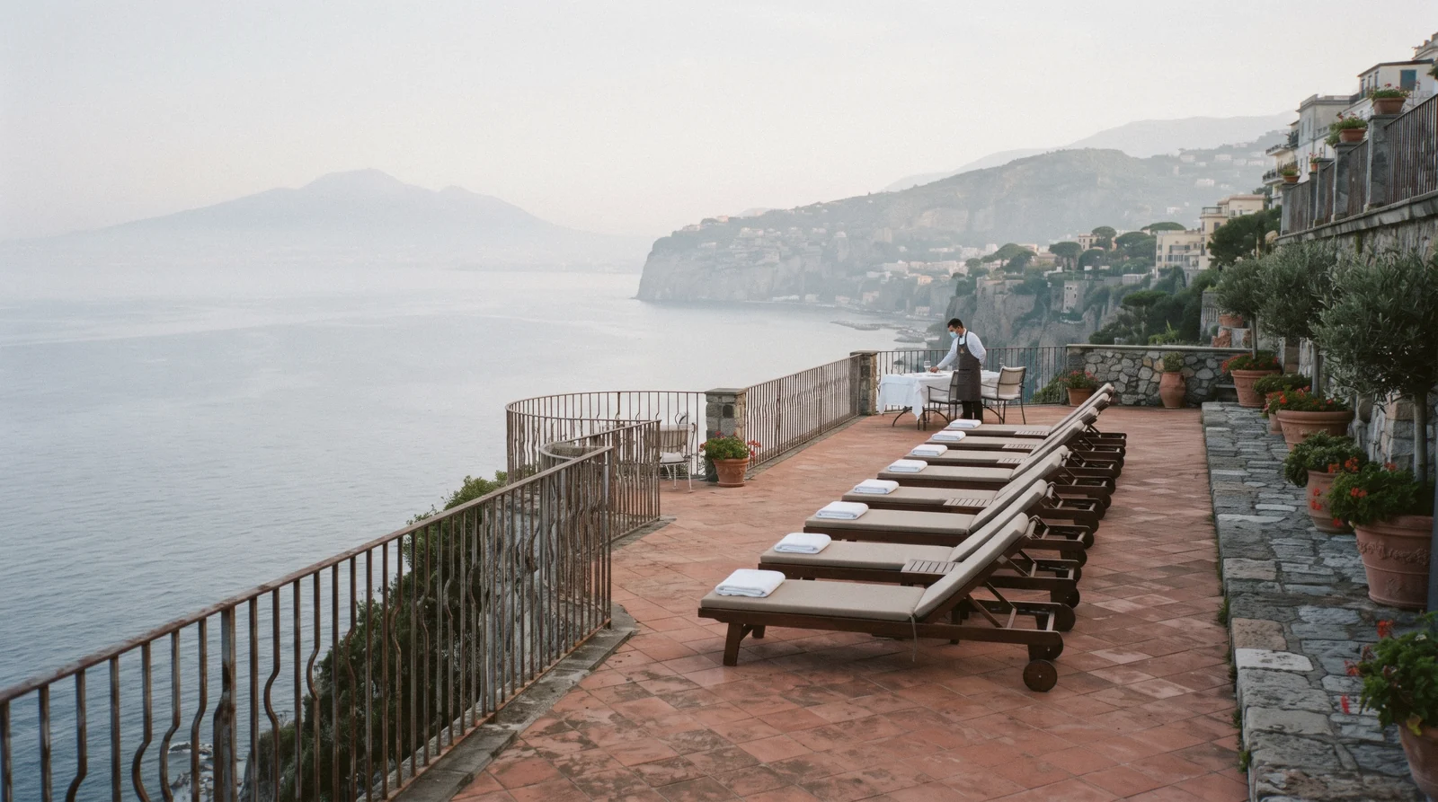A cliff-top hotel terrace in Sorrento in early morning light with empty loungers and the bay hazy below